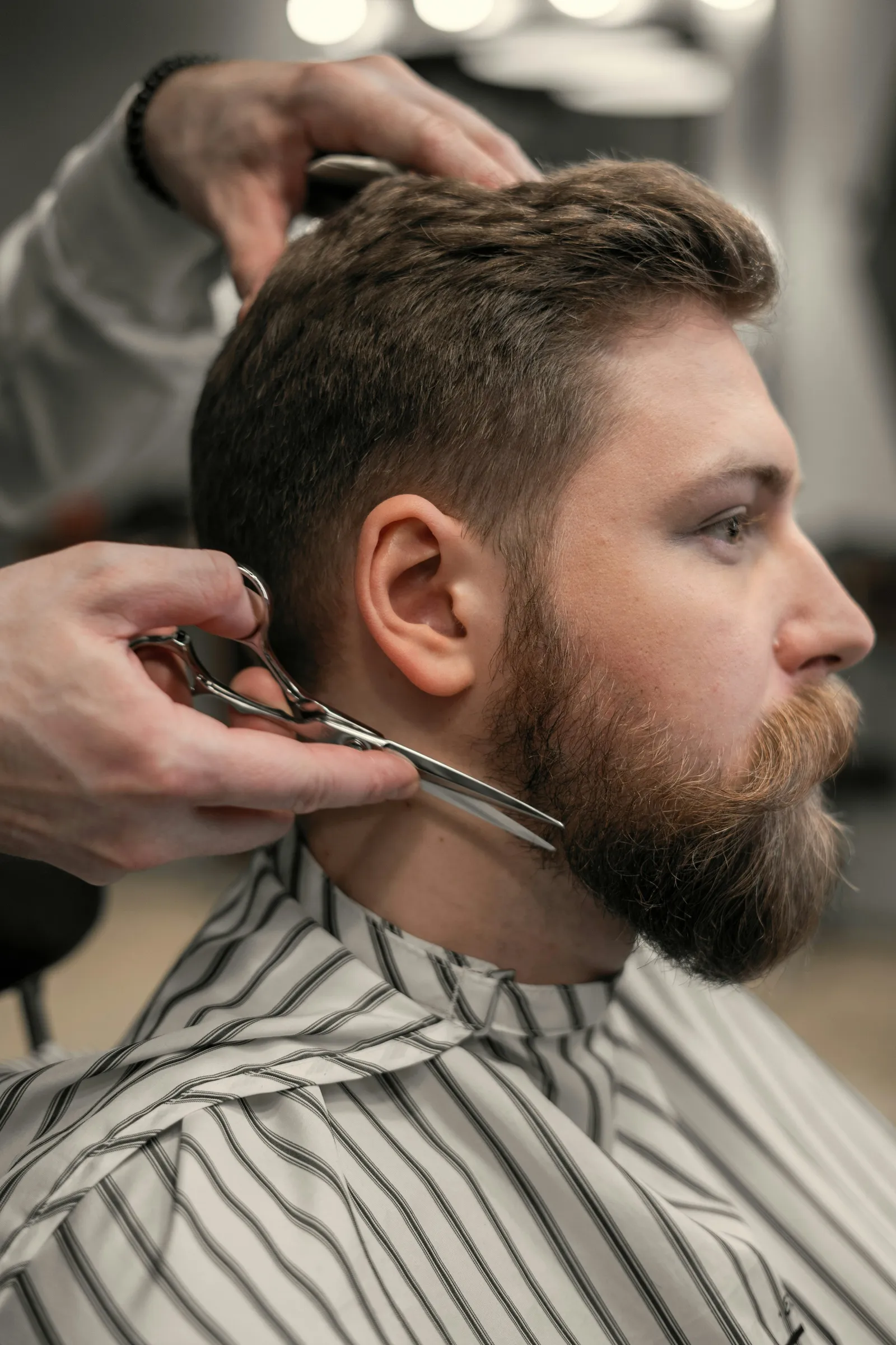 A barber trims a full beard with scissors