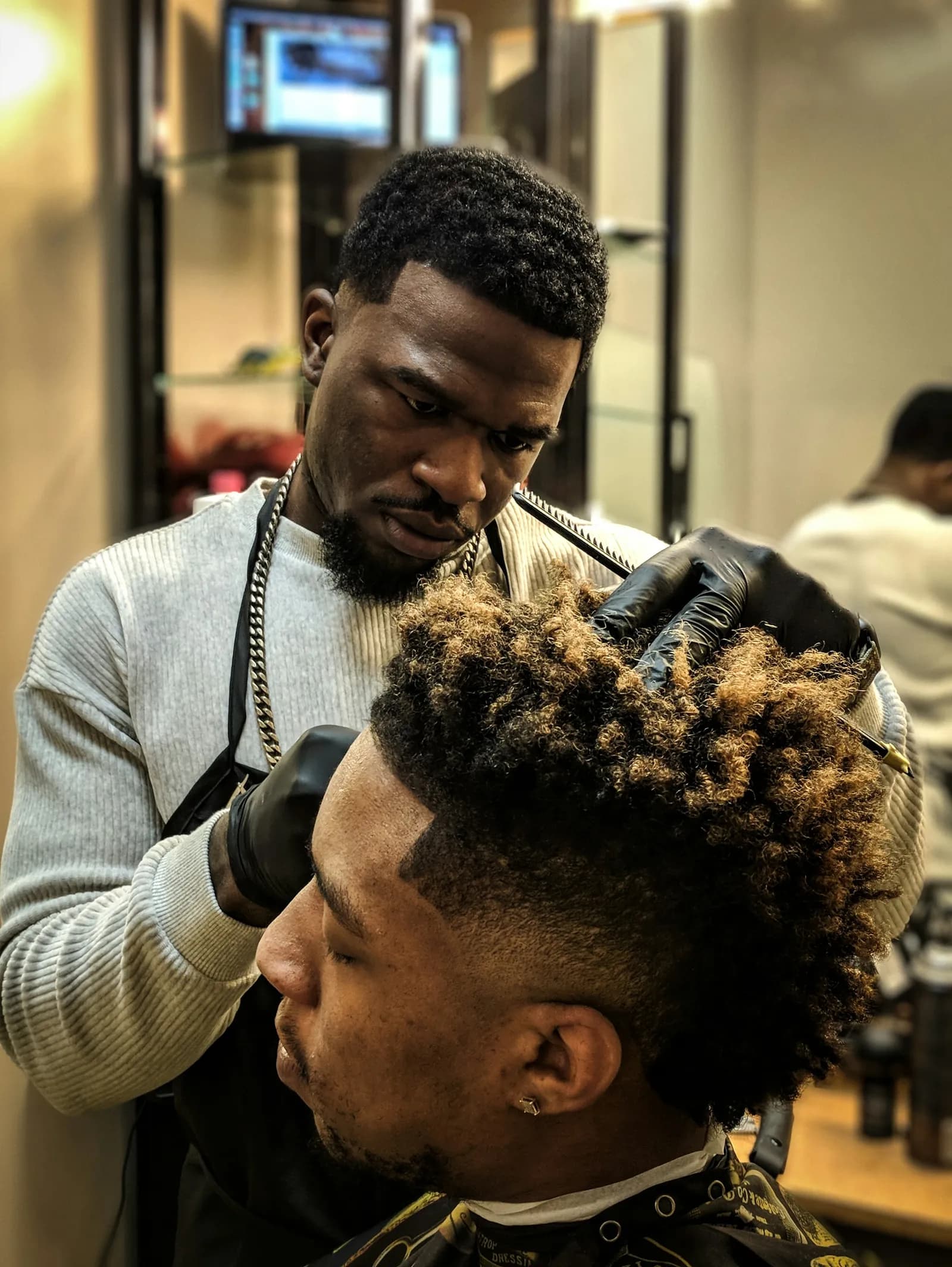 A barber in gloves cuts a fade under curly hair on top