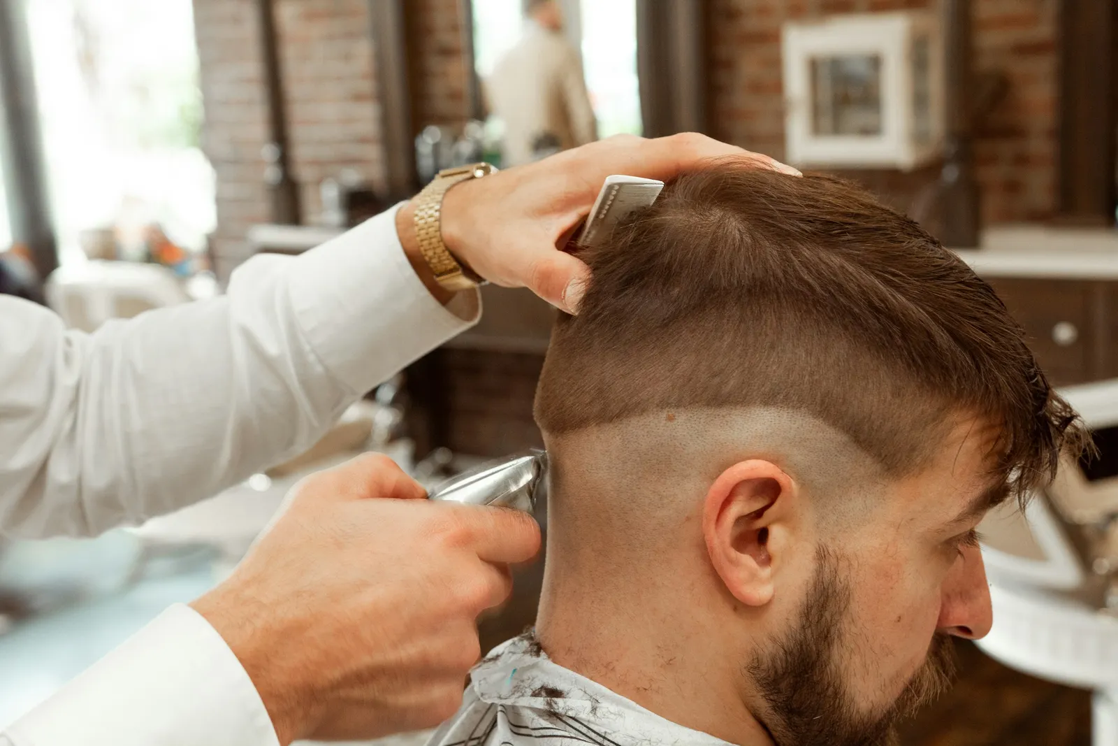 Un barbero sostiene el pelo de arriba con un peine y recorta el lado con la máquina