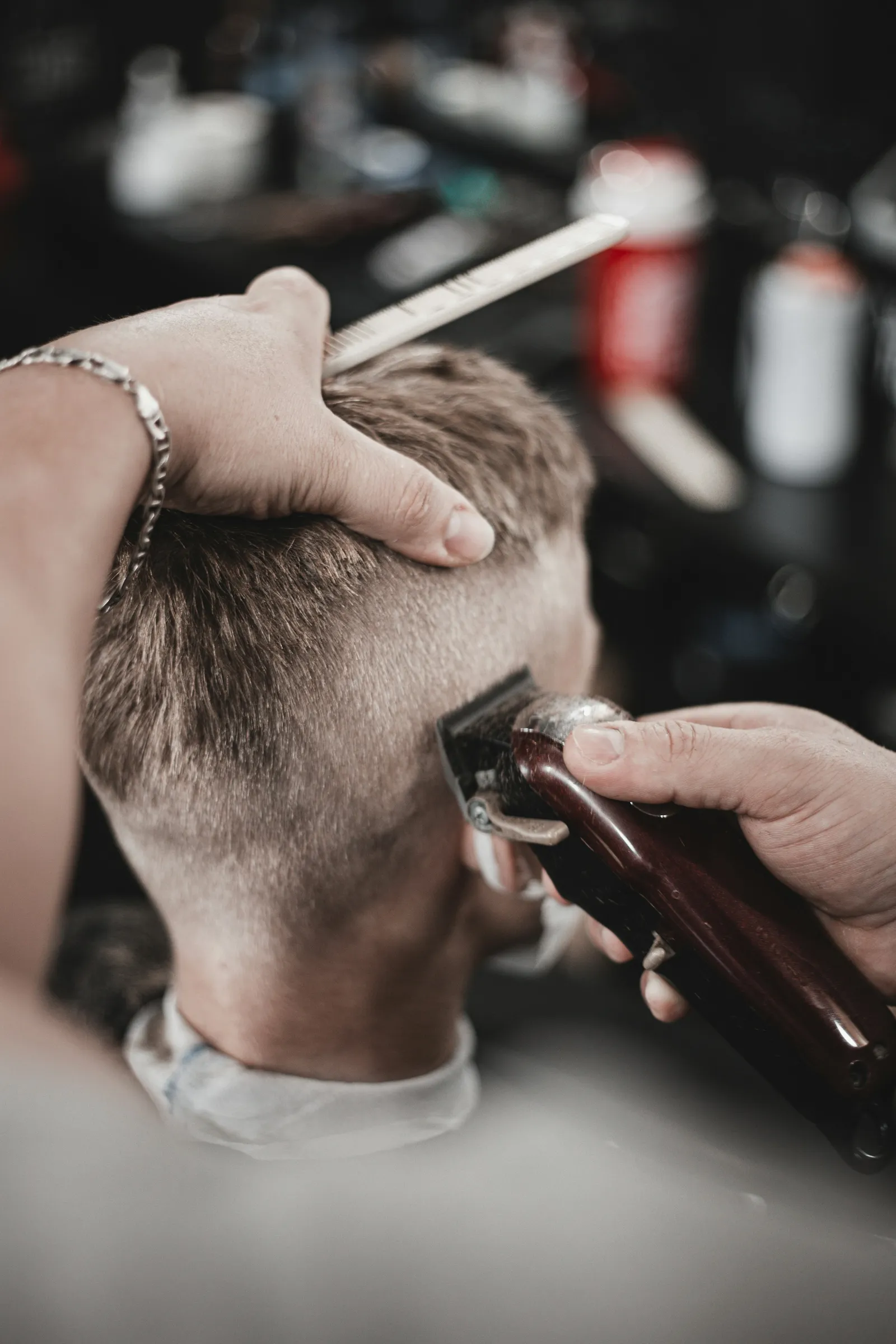 A barber holds the top up with a comb and cuts a low fade with clippers