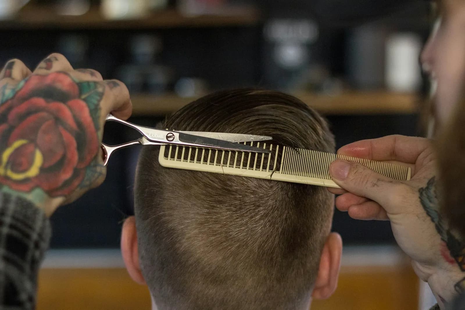 A barber cuts the back of the head with shears over a comb