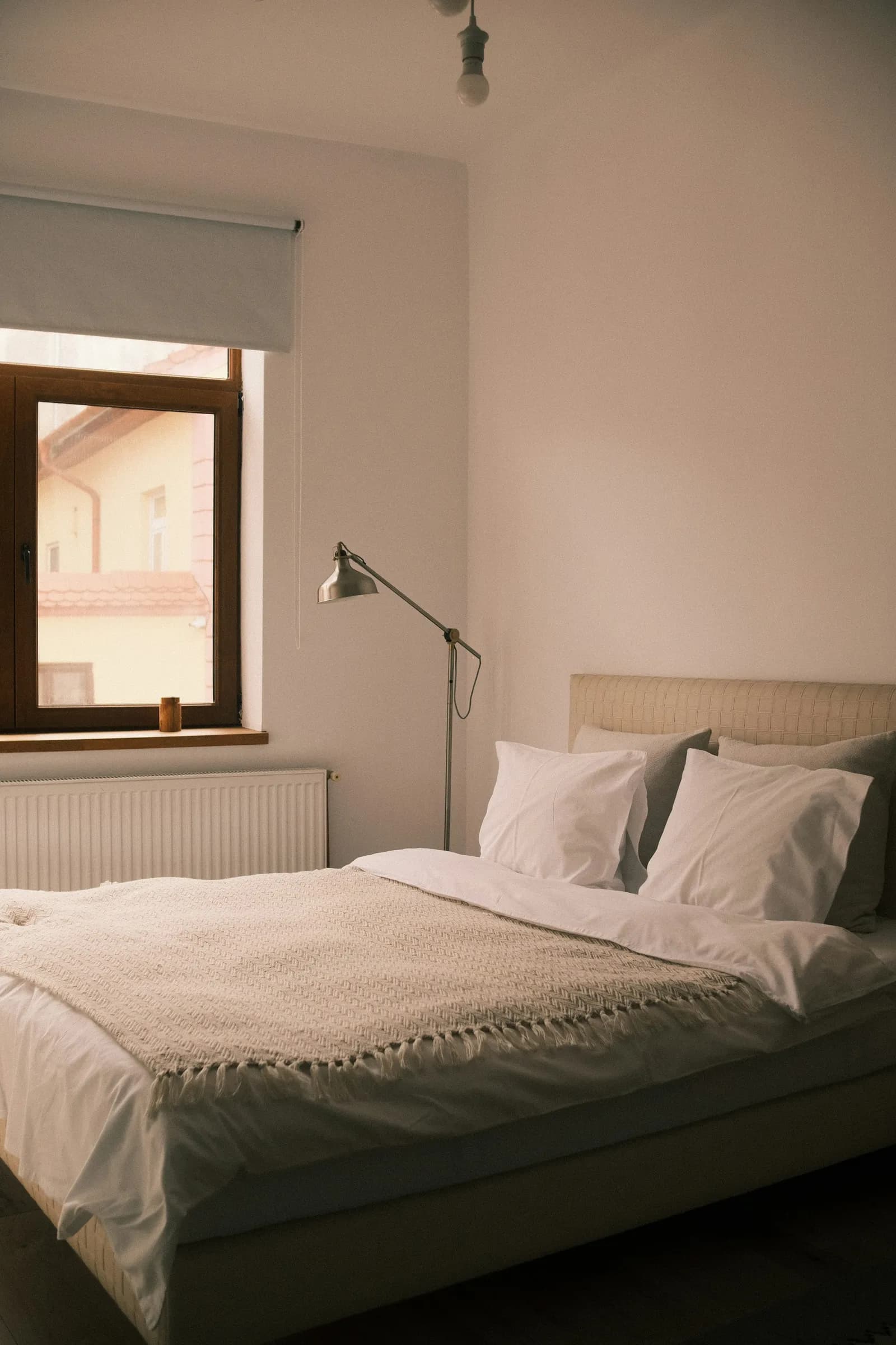 A made bed with white sheets and a soft blanket, by a window