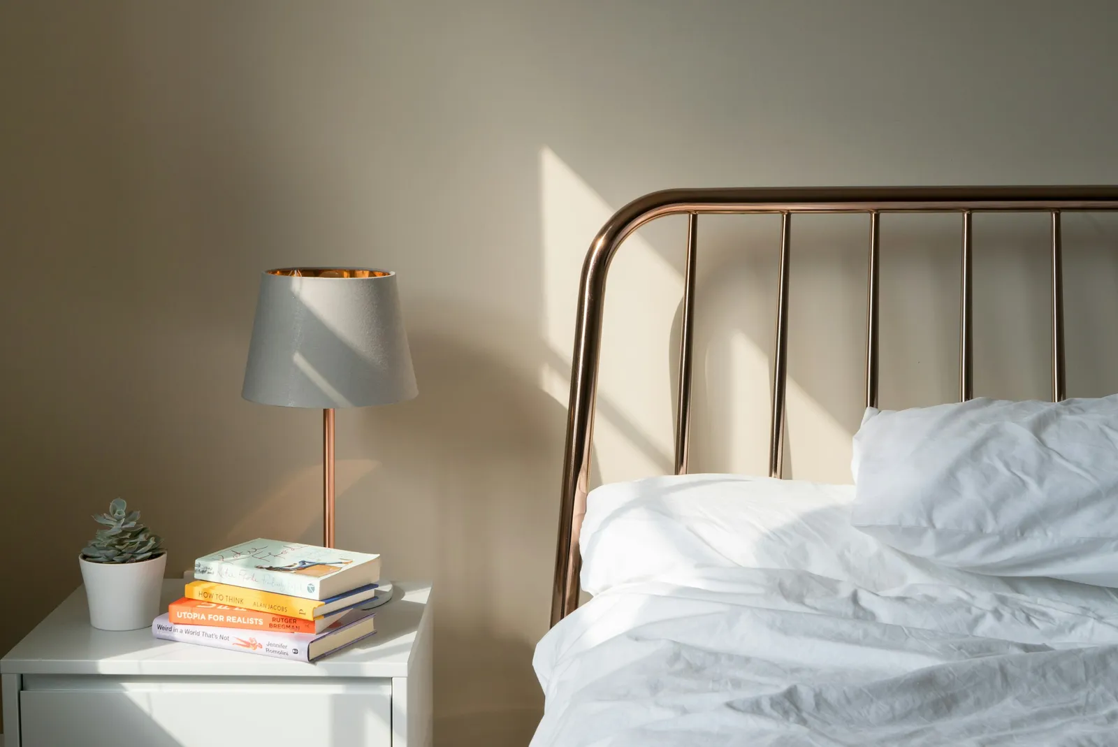A tidy nightstand with a lamp and books, next to a bed
