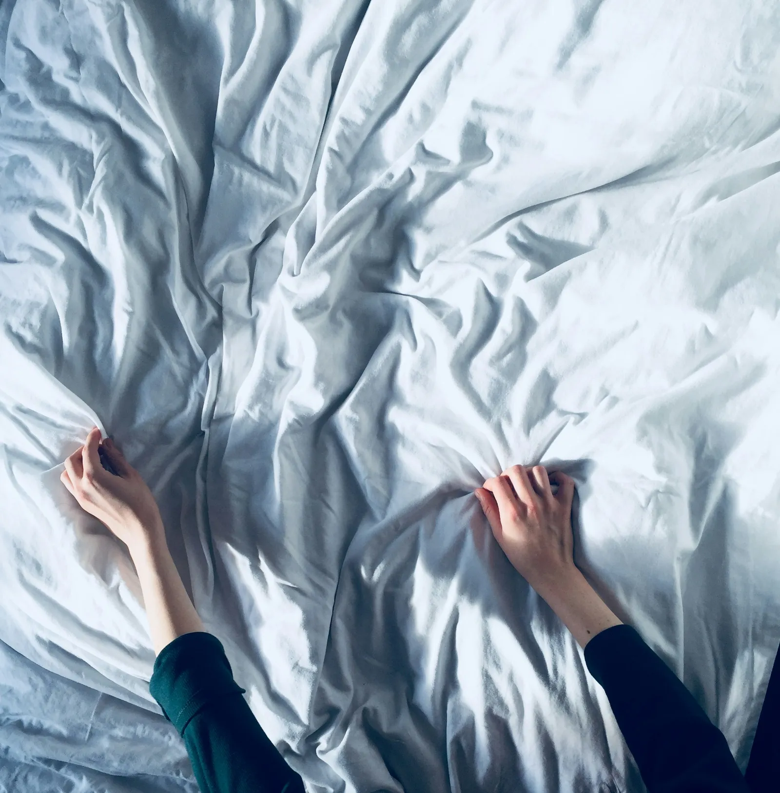 Two hands smooth a white sheet on a bed