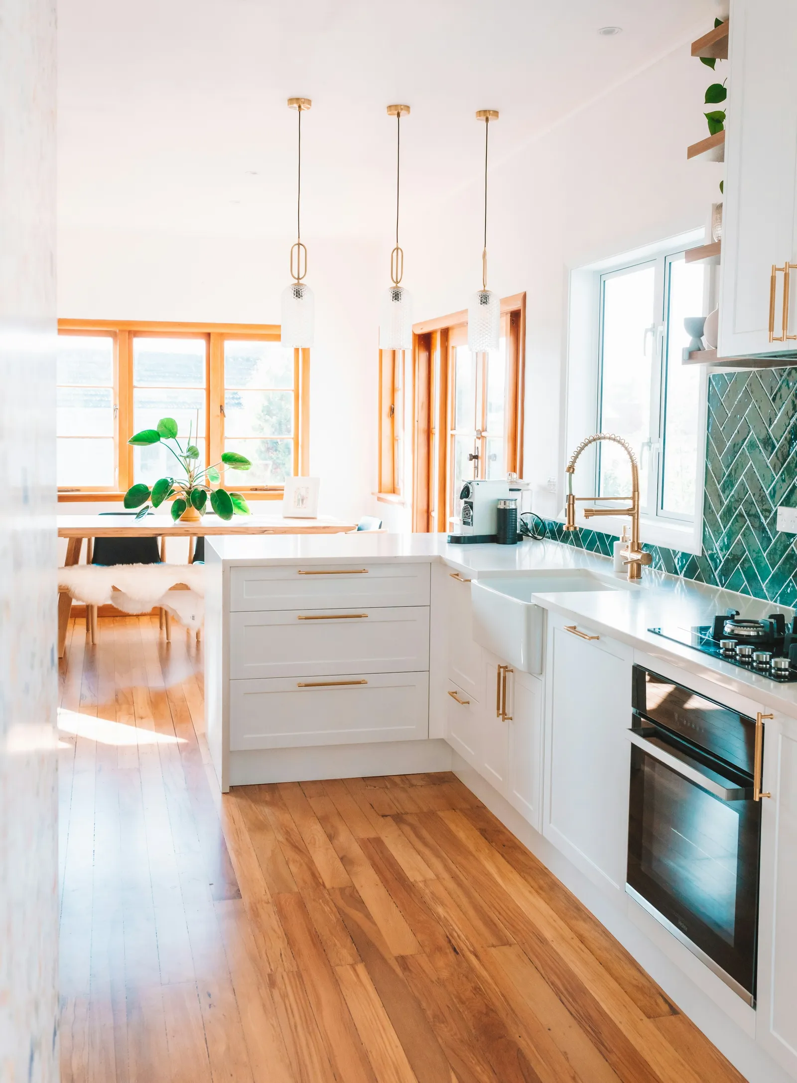 A bright white kitchen with wood floors and sun from the windows