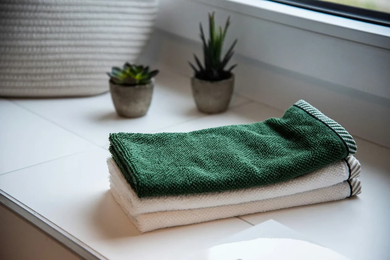 A folded green towel on white towels, next to two small plants