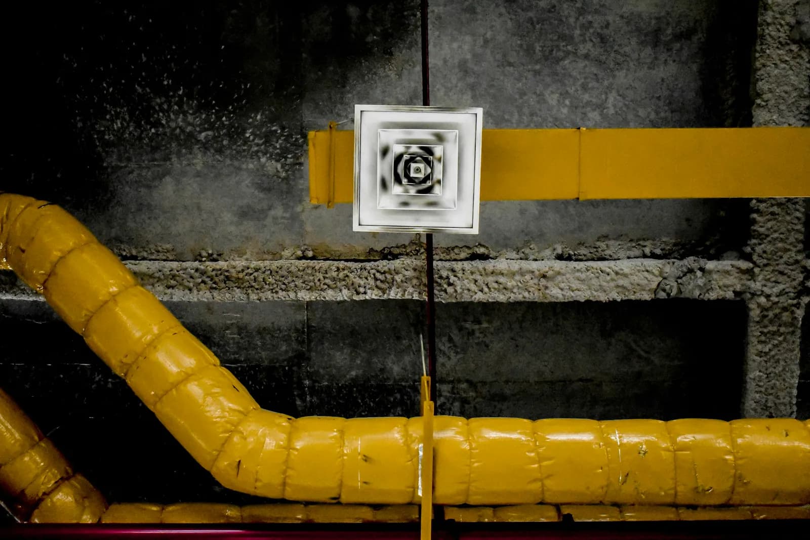 A vent and yellow wrapped air ducts on a dark wall