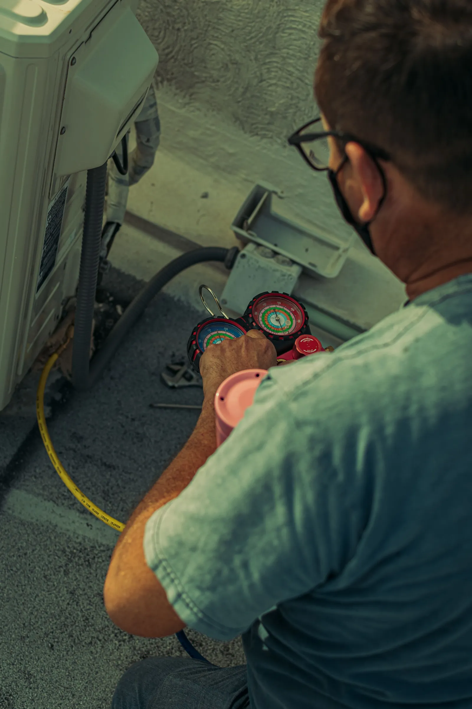A technician reads the gauges on an outdoor AC unit