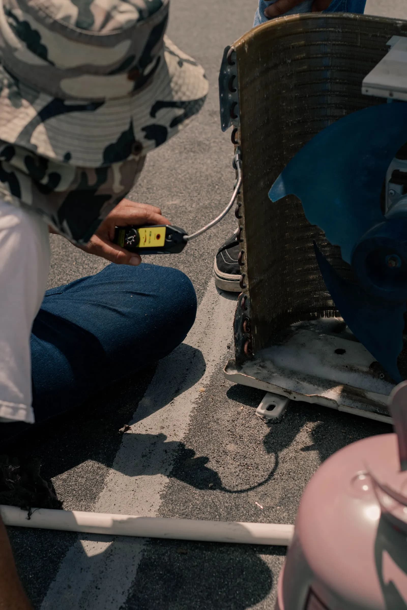 A worker checks an open AC unit with a leak tester