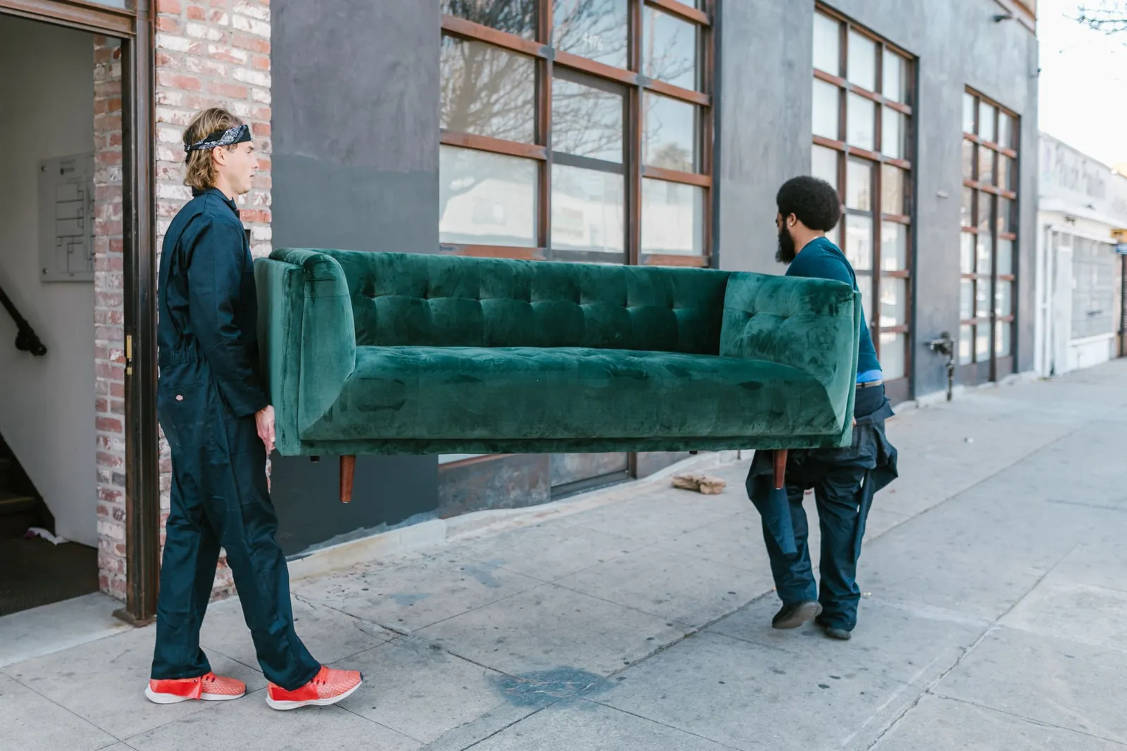 Two workers carry a green couch down the sidewalk