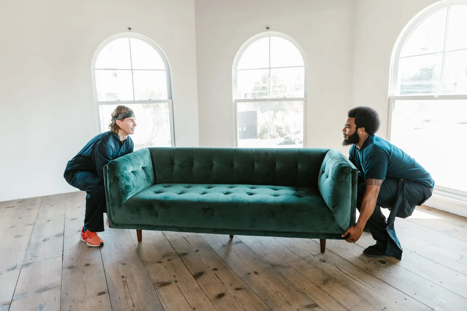 Two workers lift a green couch out of an empty room