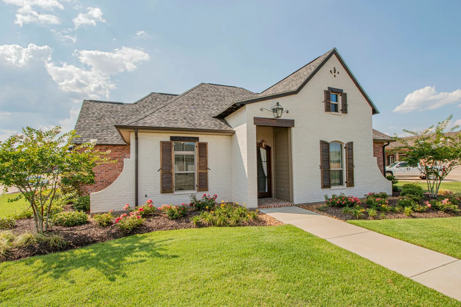 A white brick house with a green front lawn, trimmed shrubs and flower beds