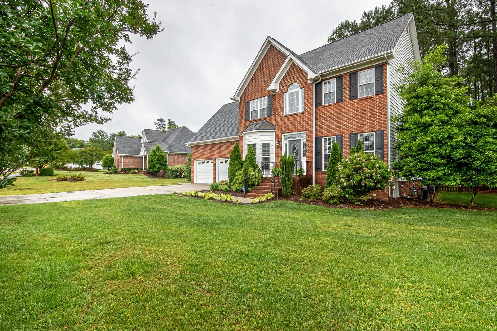 A red brick house with a wide green lawn and shrubs along the front