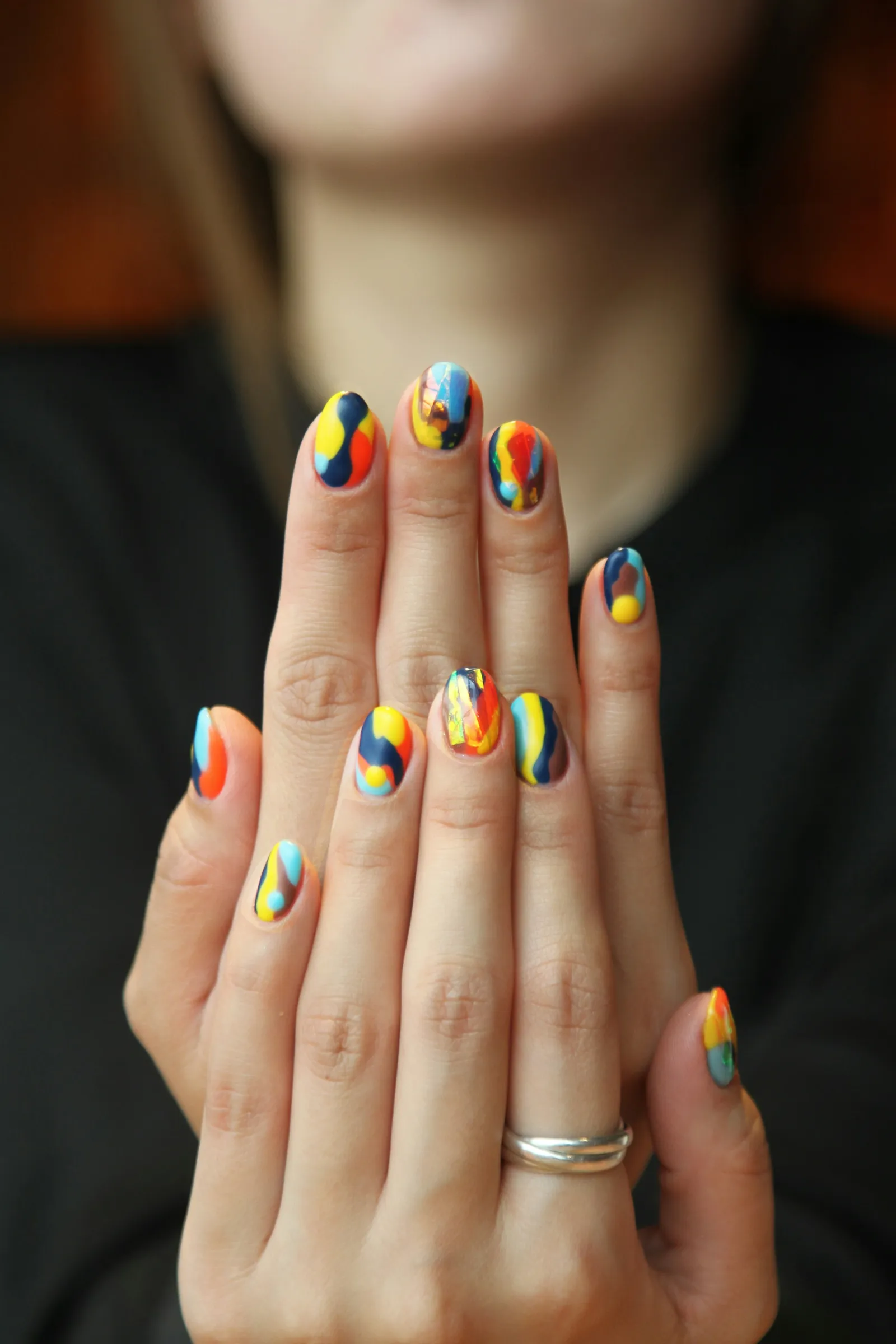 Two hands with bright nail art in blue, yellow and red swirls