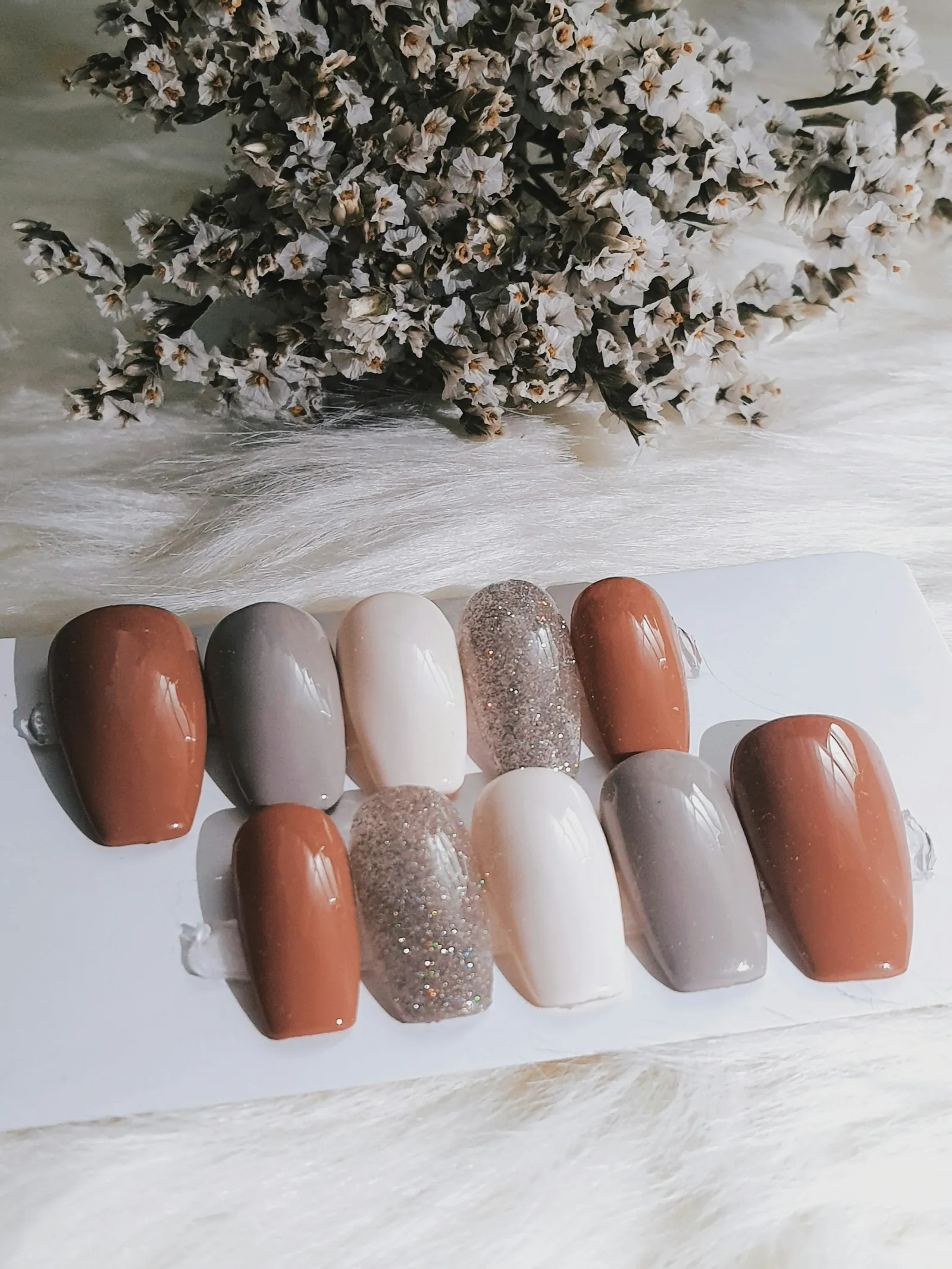 Nail tips in brown, gray, white and glitter, laid out like swatches