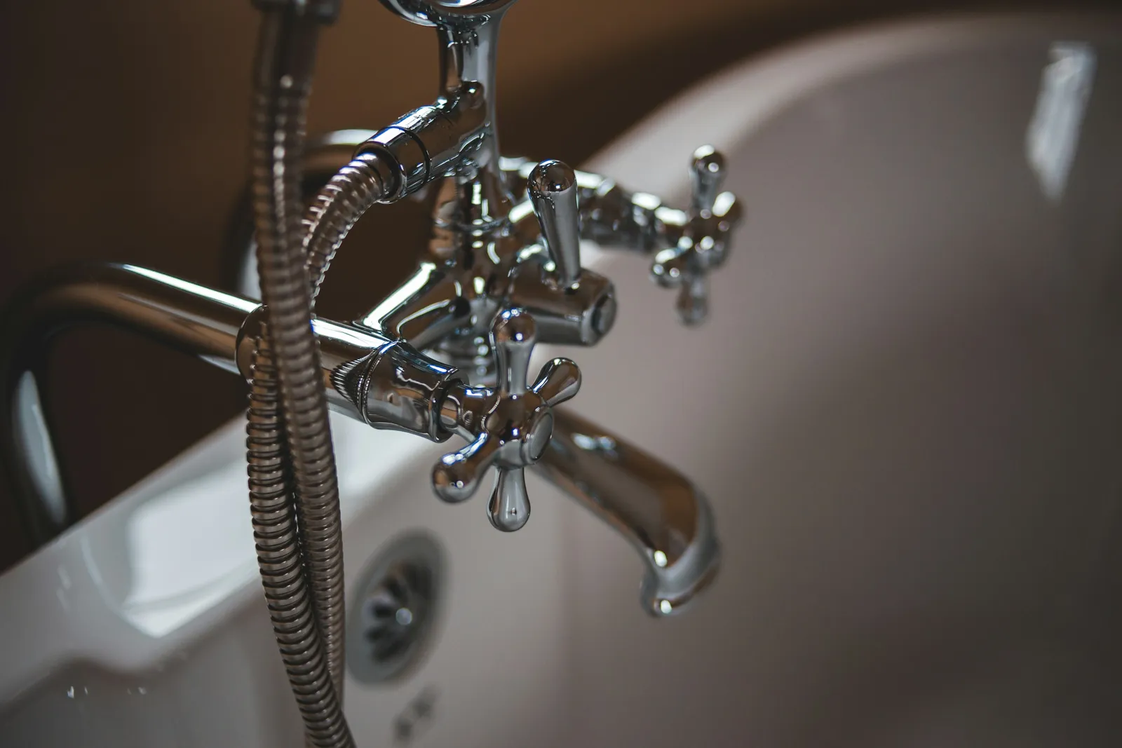 A chrome faucet and shower hose over a white tub