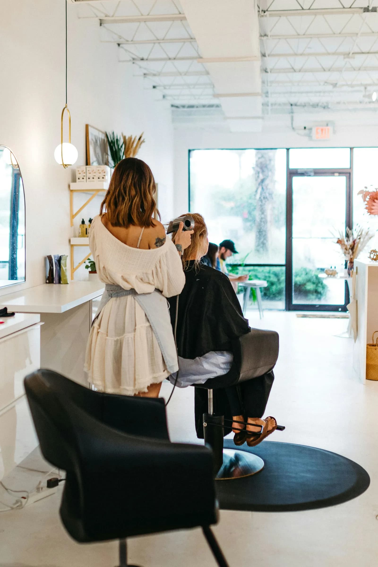A stylist works on a client in a bright salon with big windows