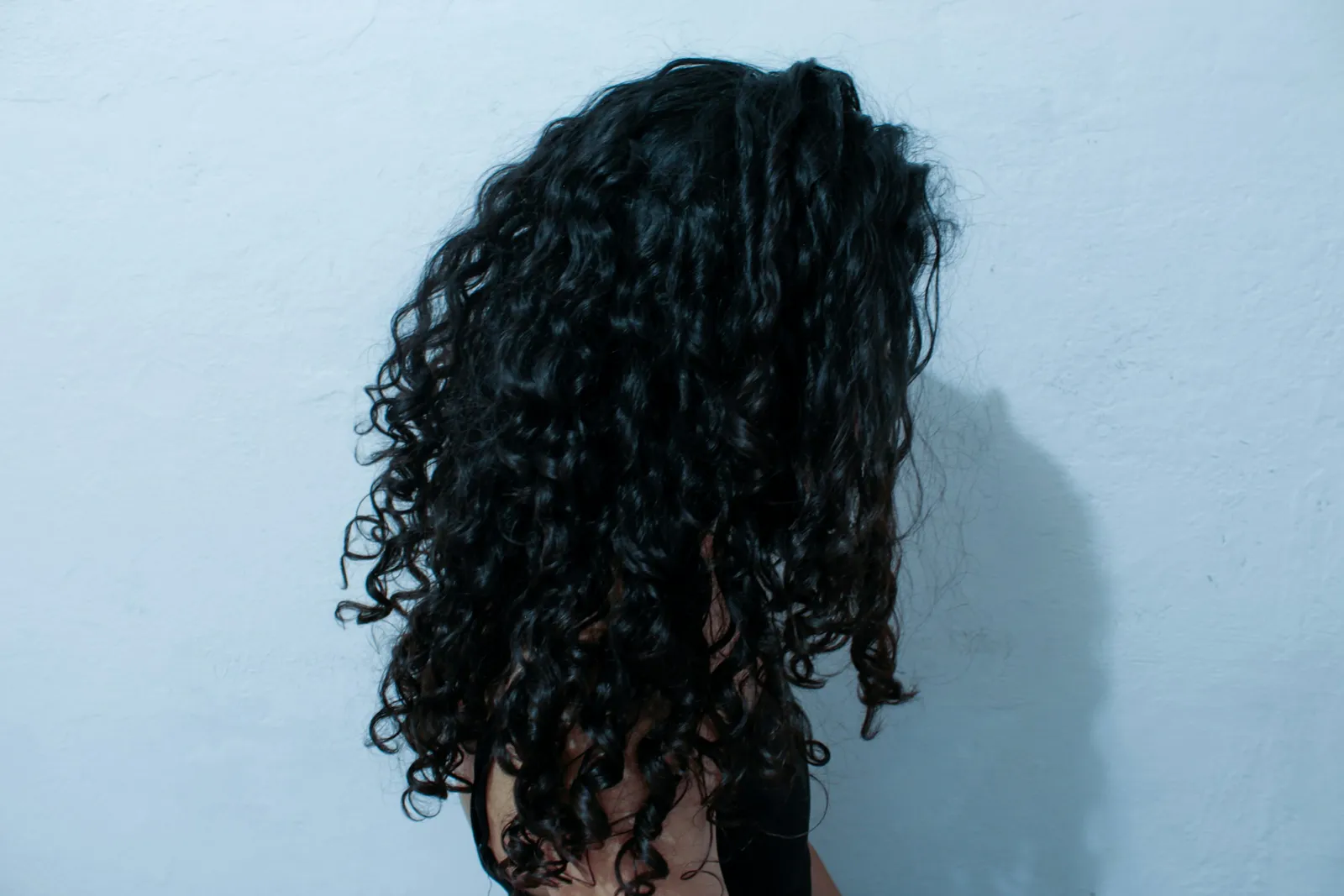 Long dark curls, seen from the back by a blue wall